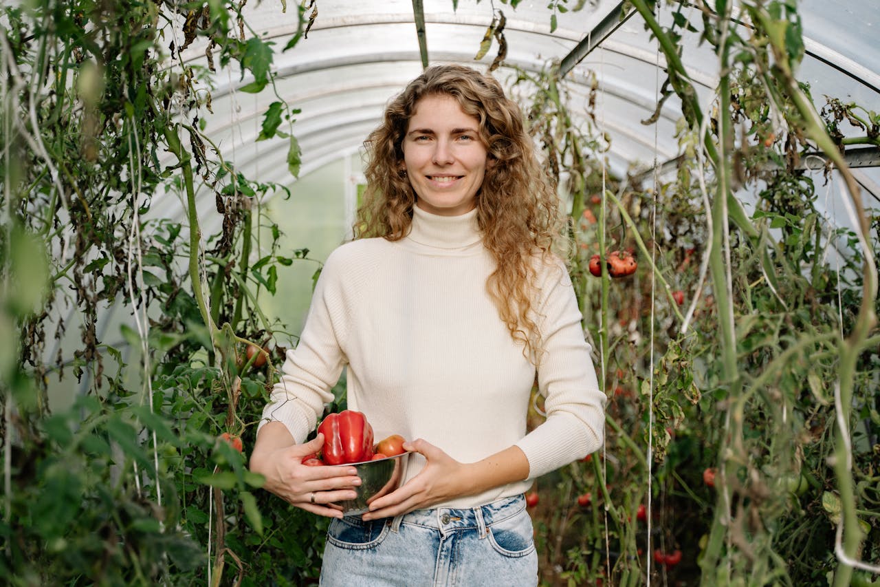 A happy woman in a greenhouse holding freshly harvested organic red bell peppers.
