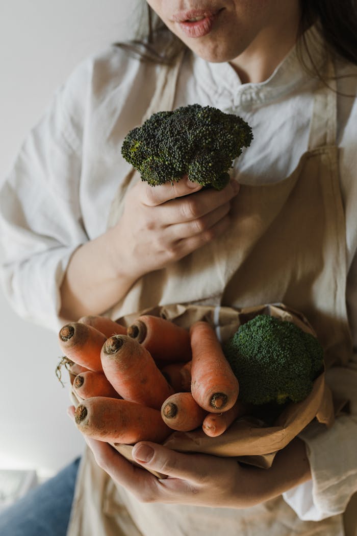 Woman holding fresh broccoli and carrots, emphasizing healthy eating and natural produce.